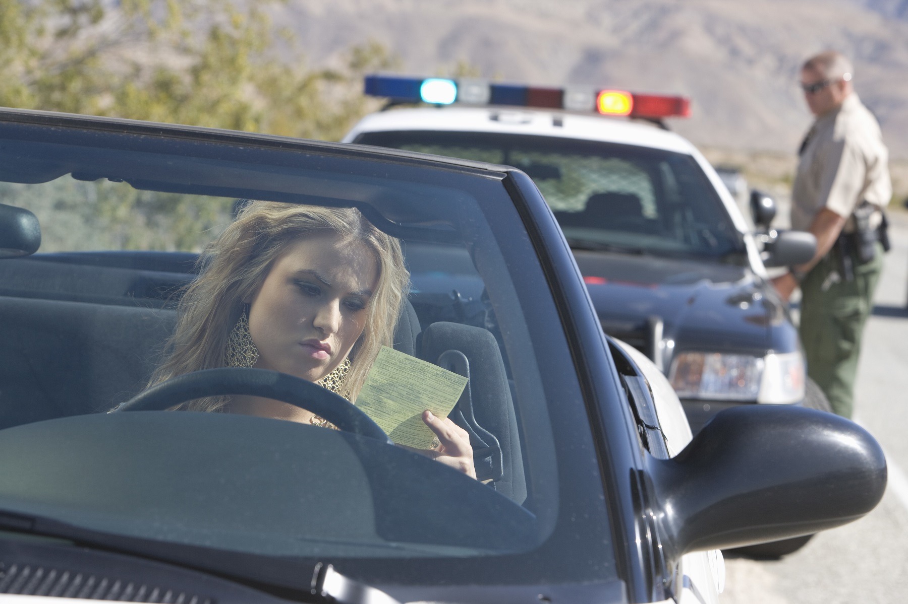 Young woman in car reading ticket with traffic cop in the background Young woman in car reading ticket with traffic cop in the background